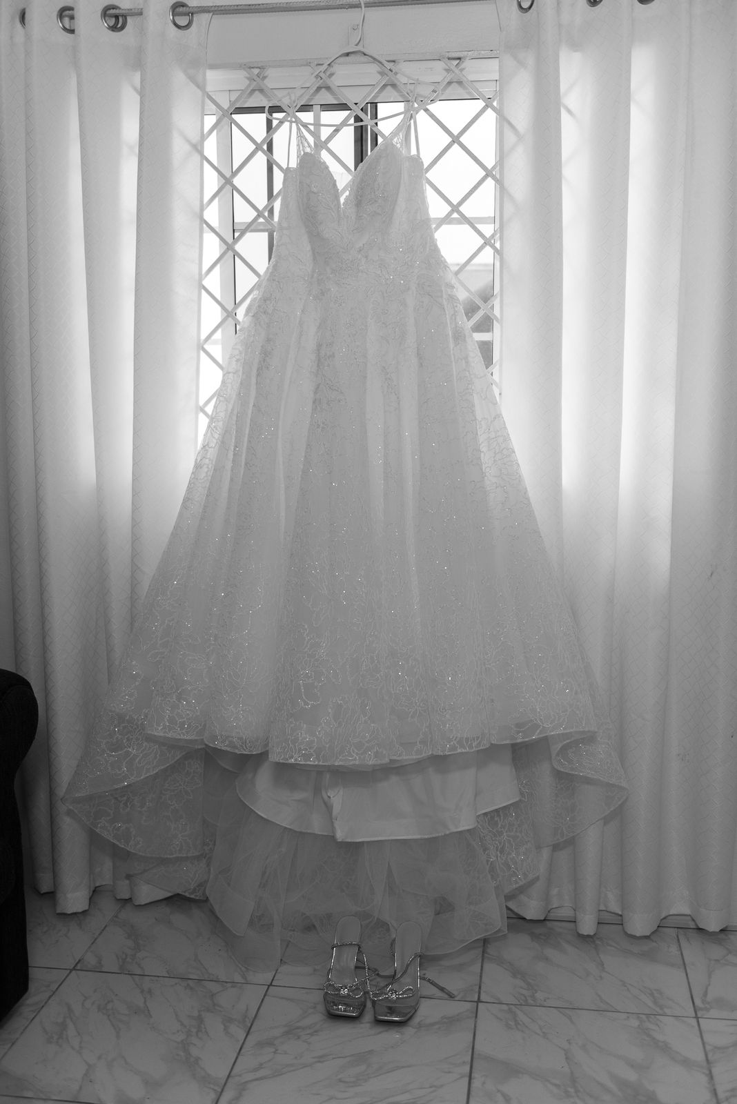 A wedding dress hanging in a doorway against bright curtains, in black and white