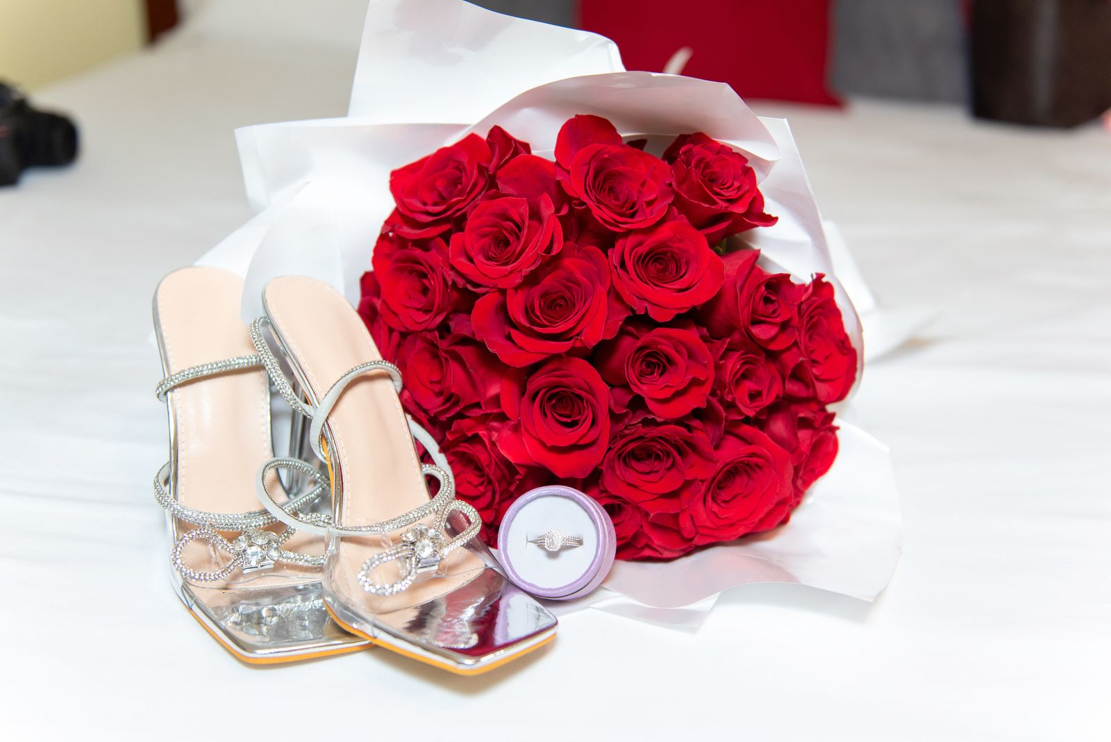 Silver bridal shoes beside a bouquet of red roses and the wedding ring