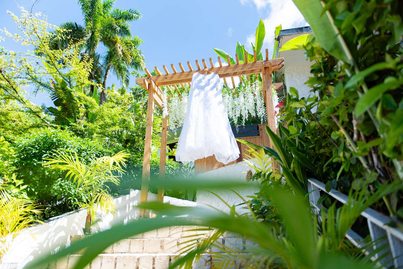 The wedding dress hanging from a wooden pergola in a tropical garden