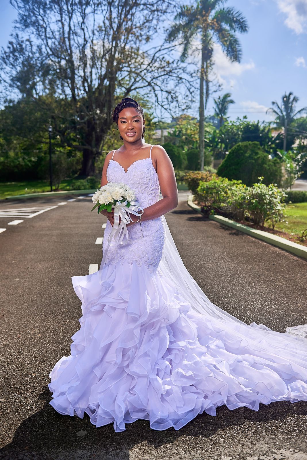 The bride on a palm-lined driveway, her ruffled train spread behind her