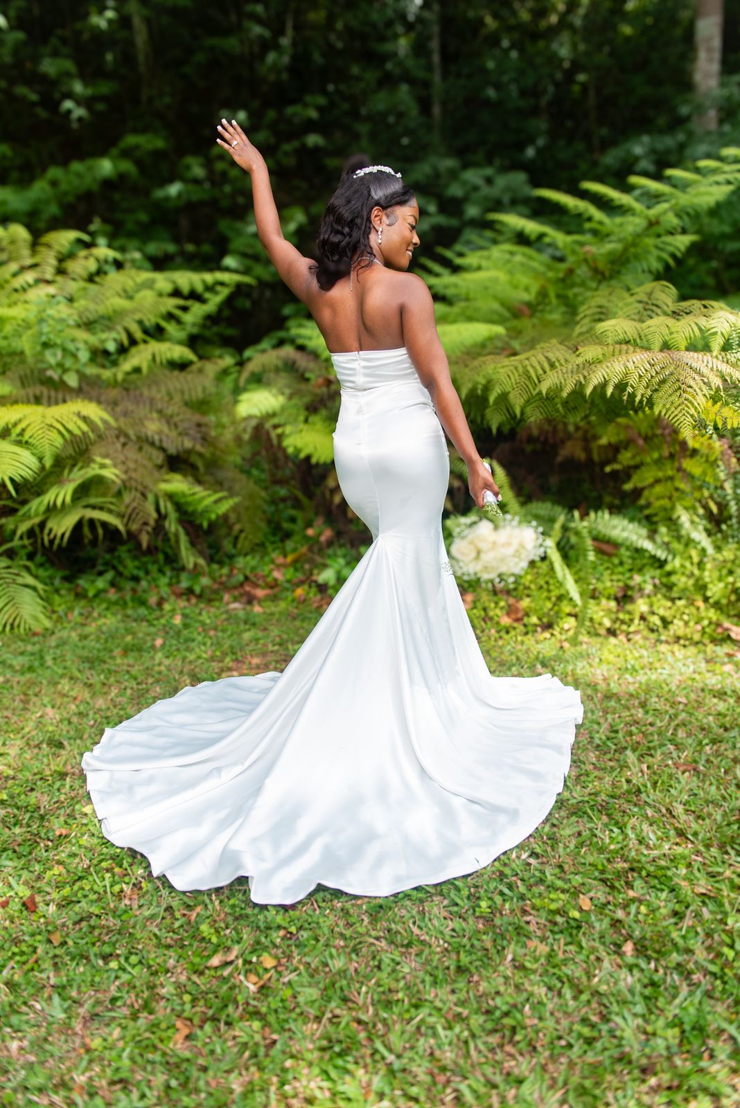 The bride turning with one arm raised, her train sweeping across the grass