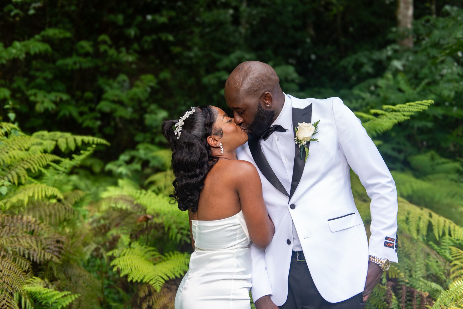 The groom leaning in to the bride among tree ferns, both mid-laugh