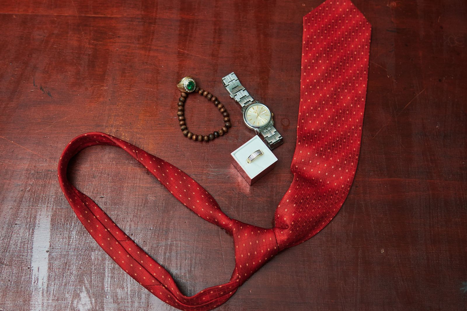 The groom's red tie, watch and beaded bracelet laid out on dark wood