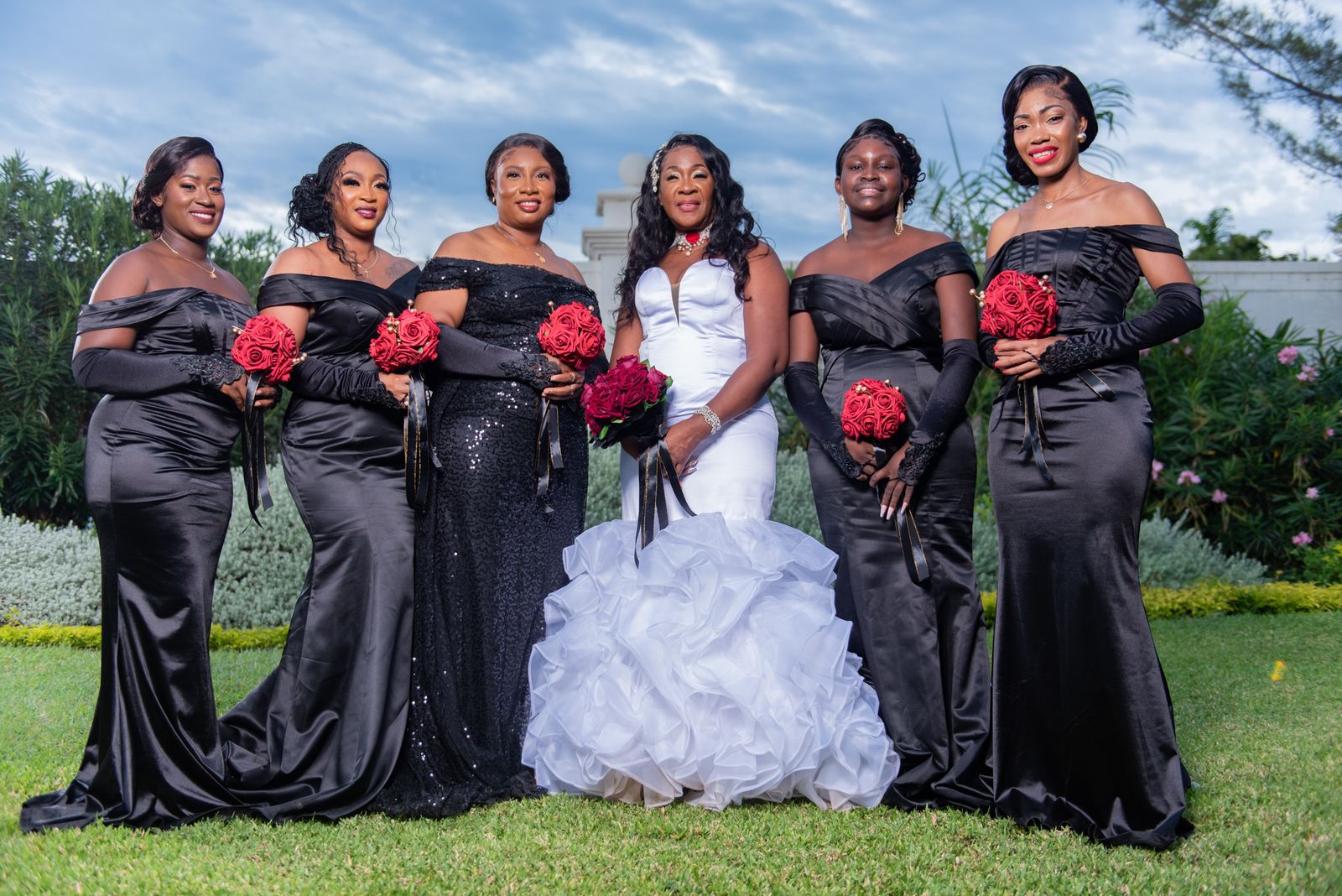 The bride with her bridesmaids in black gowns holding red bouquets