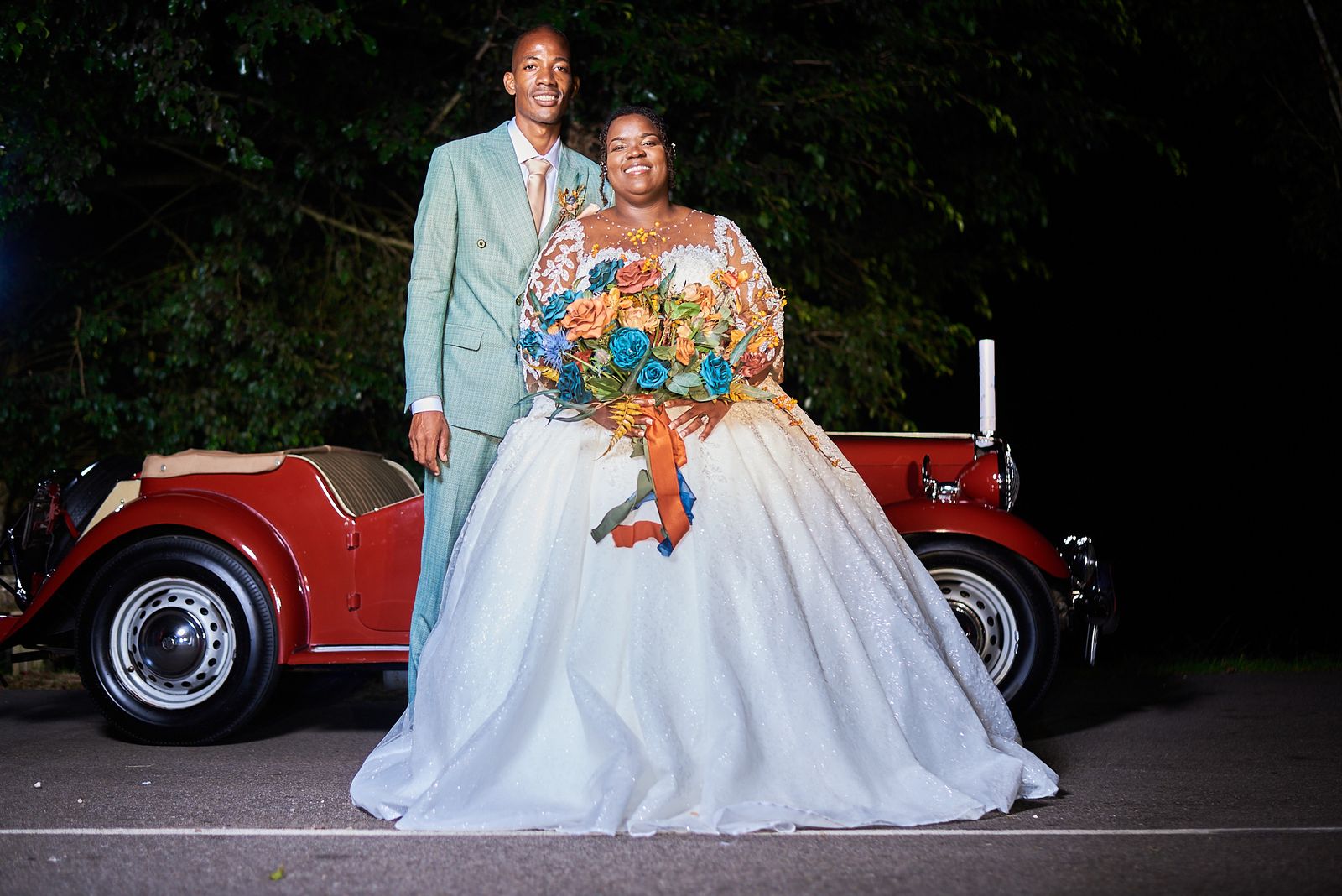 The couple beside a red classic convertible at night