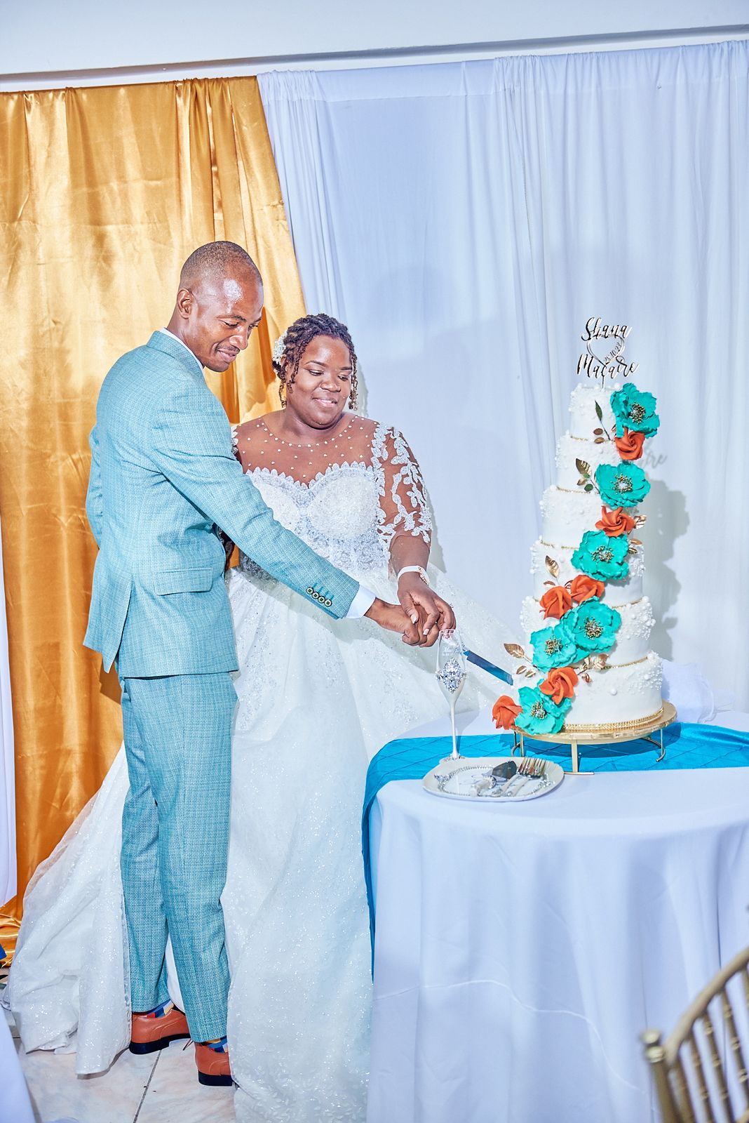 The couple cutting a tiered cake decorated with teal and orange flowers