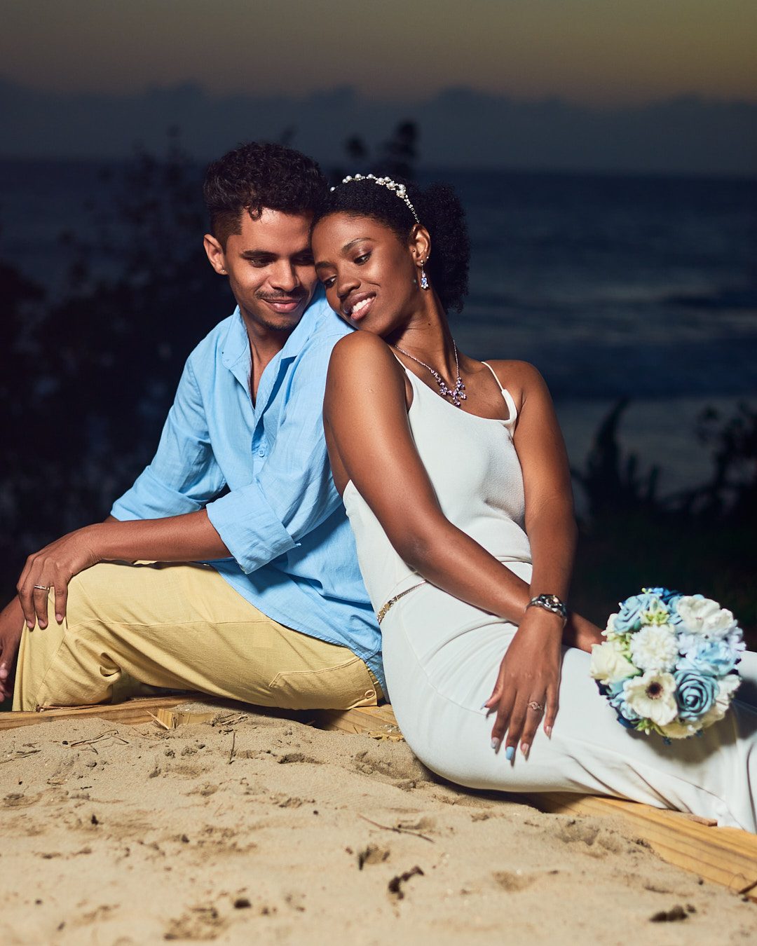 A couple sitting together on the sand at dusk
